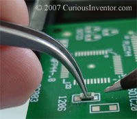 Curved tweezers holding a 1206 resistor